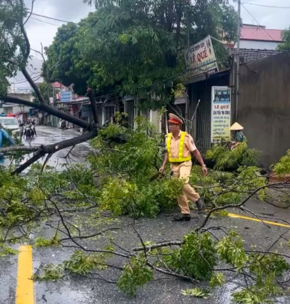 Cảnh sát giao thông cùng người dân dọn dẹp cây đỗ chắn ngang đường, giúp phương tiện lưu thông an toàn.