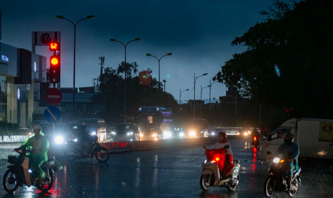 Hà Nội bầu trời tối đen, mưa tầm tã, sấm chớp đì đùng, phương tiện di chuyển chậm chạp, nhiều ánh đèn xe le lói giữa màn mưa.