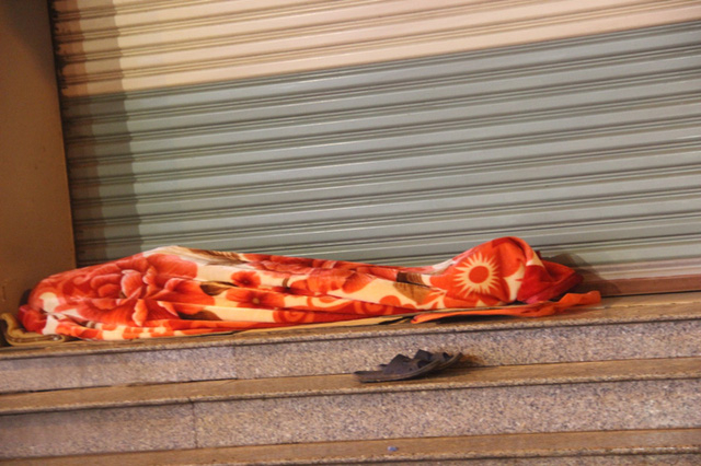 Một người t&igrave;m cho m&igrave;nh giấc ngủ cạnh quầy h&agrave;ng, b&ecirc;n h&agrave;nh lang đường phố.