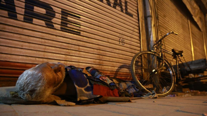 Một người cao tuổi qua đ&ecirc;m trước cửa một cửa h&agrave;ng tạp h&oacute;a tại khu Paharganj b&ecirc;n chiếc xe đạp cũ kĩ. (Ảnh: AMAL KS/HT)