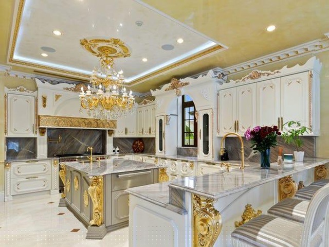 Trong gian bếp, nổi bật ở giữa là bàn bếp được ốp đá cẩm thạch, nhiều chi tiết trang trí màu vàng sang chảnh. Các tủ bếp xung quanh vẫn giữ màu sơn trắng là chủ đạo, cùng với quầy bar nhỏ vẫn giữ được nét hiện đại.