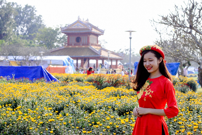 Duy&ecirc;n d&aacute;ng trong t&agrave; &aacute;o d&agrave;i b&ecirc;n cạnh những chậu hoa c&uacute;c rực rỡ.