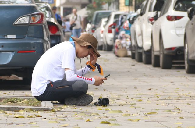 Một ph&oacute;ng vi&ecirc;n ngồi nghỉ tr&ecirc;n vỉa h&egrave; phố Ng&ocirc; Quyền trong l&uacute;c chờ đợi sự kiện diễn ra.