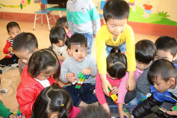 Ch&aacute;u H. mặc &aacute;o x&aacute;m, tay cầm đồ chơi với c&aacute;c bạn. (Ảnh: Ba Zin/Baolaocai)