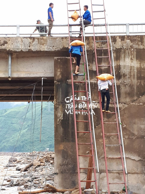 Từ l&ograve;ng suối l&ecirc;n mặt cầu cao h&agrave;ng chục m&eacute;t, thanh ni&ecirc;n vừa c&otilde;ng gạo, vừa phải leo thang.