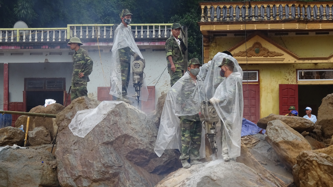 Lực lượng cứu hộ đang dầm mưa ph&aacute; những khối đ&aacute; tảng nặng h&agrave;ng chục tấn được lũ qu&eacute;t đẩy về thị trấn M&ugrave; Cang Chải.