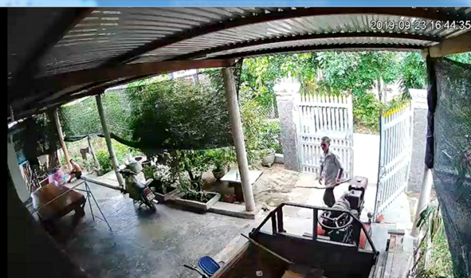 Ông Nguyễn Văn Trí cầm cây bước vào nhà ông Lê Anh khi chủ nhà đang ngồi ở góc sân. Ảnh : cắt từ camera gia đình ông Lê Anh