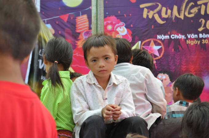 Một em học sinh lớp tiểu học ngồi dưới s&acirc;n trường c&ugrave;ng c&aacute;c bạn chờ đến tối để đ&oacute;n Trung Thu.