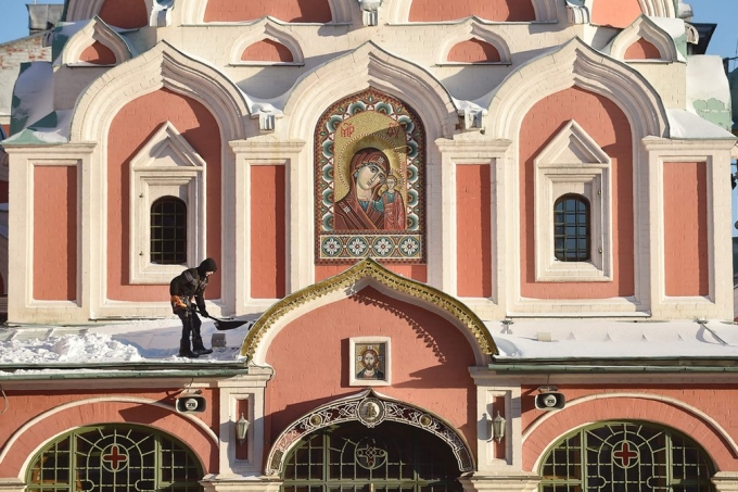 Ảnh một người đ&agrave;n &ocirc;ng lấy xẻng x&uacute;c tuyết đọng lại tr&ecirc;n m&aacute;i của một nh&agrave; thờ tại Quảng trường Đỏ, Moscow. (Ảnh: Natalia Kolesnikova / AFP / Getty Images)