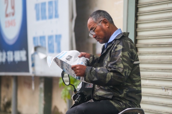 Tr&ecirc;n đường Ho&agrave;ng Sa, b&aacute;c xe &ocirc;m mặc th&ecirc;m &aacute;o ấm, thảnh thơi đọc b&aacute;o buổi s&aacute;ng trong l&uacute;c chờ kh&aacute;ch.